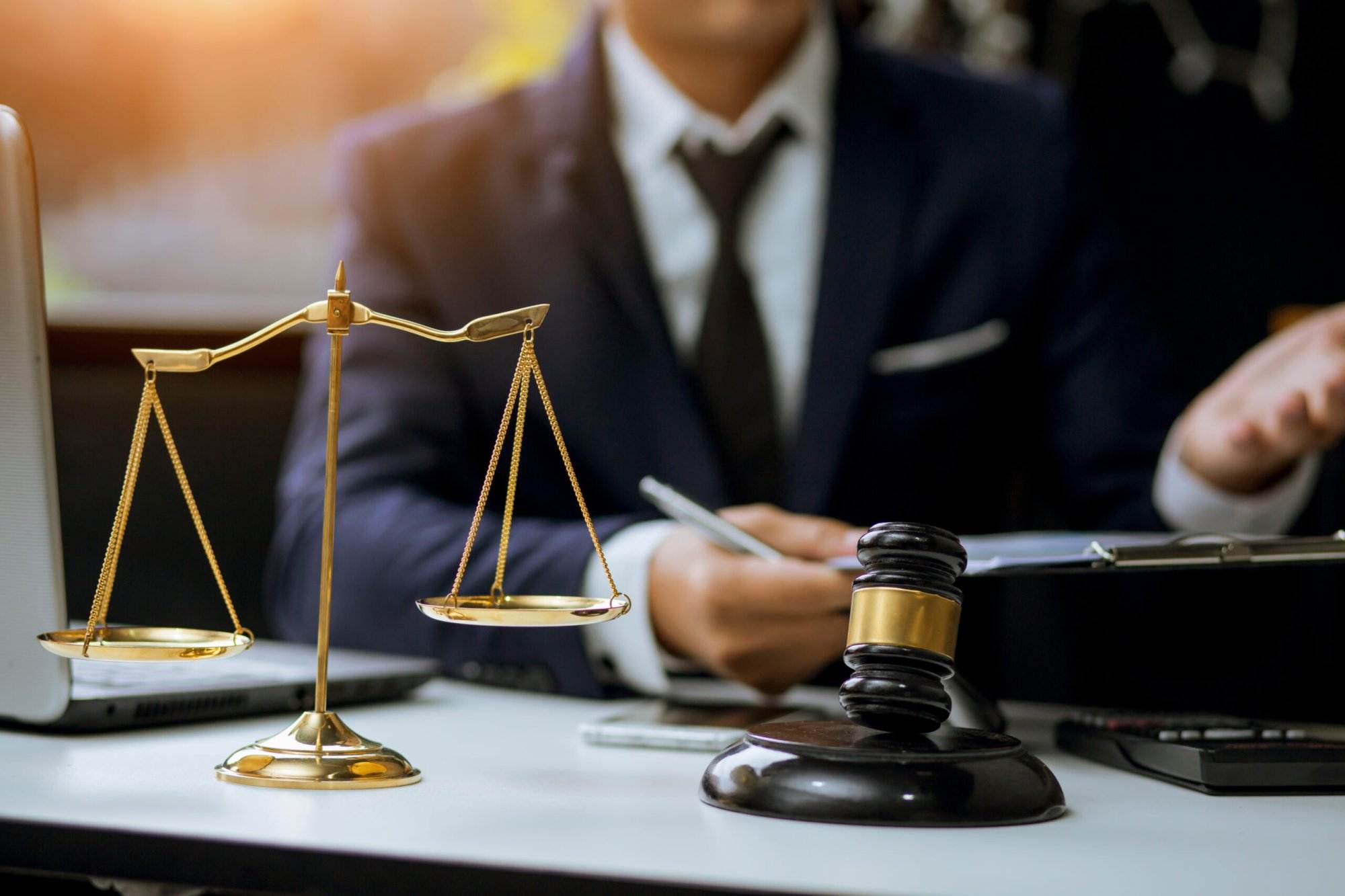 Lawyer in suit with golden scales and gavel on desk in office.