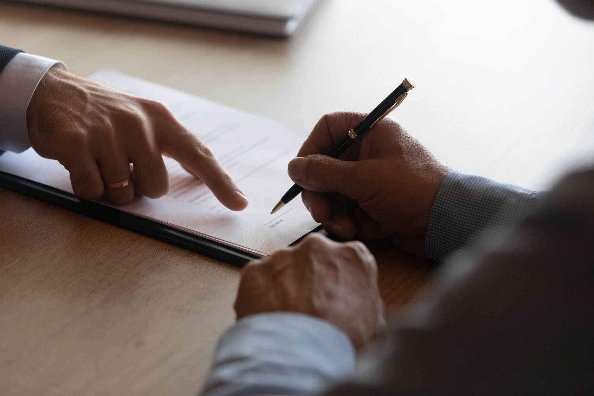 Hands signing a legal document on a wooden table, emphasizing collaboration in a formal setting.