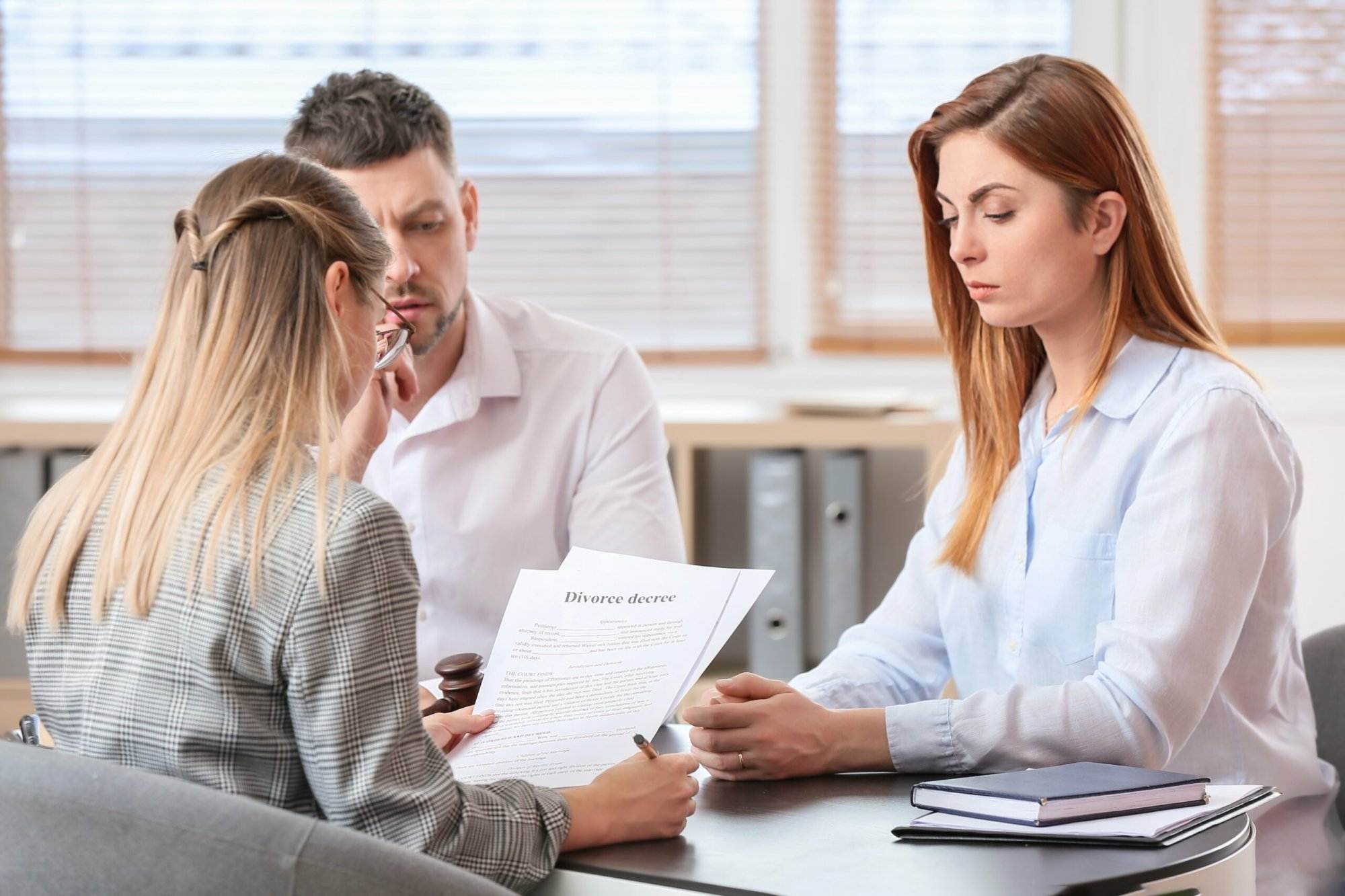 Three individuals discussing divorce papers at a table, focusing on the document with a serious and thoughtful demeanor.
