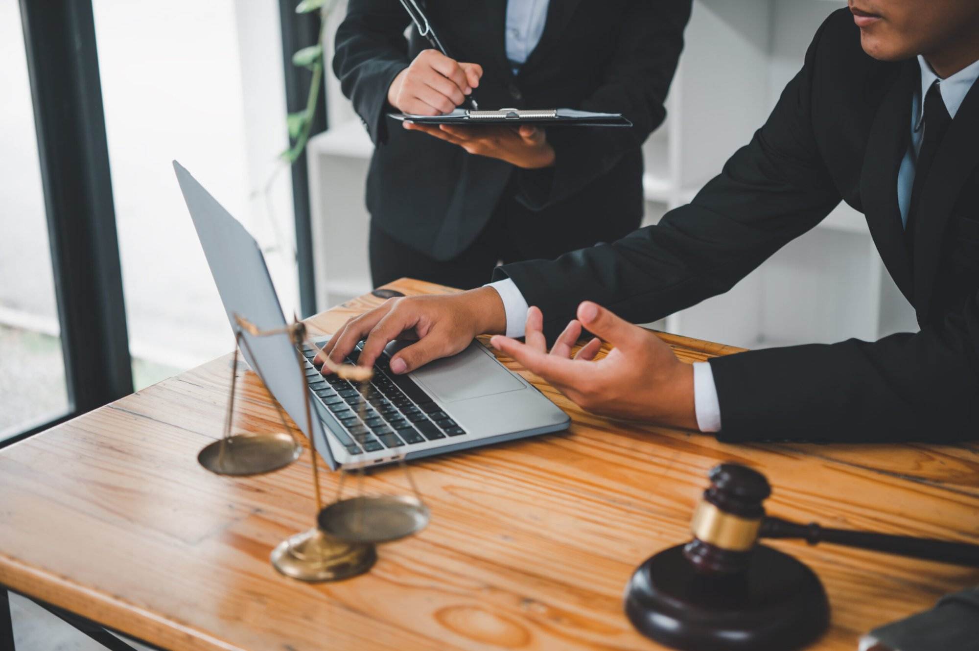 Lawyers discussing a case with a laptop and gavel on a wooden table, symbolizing modern law and justice.