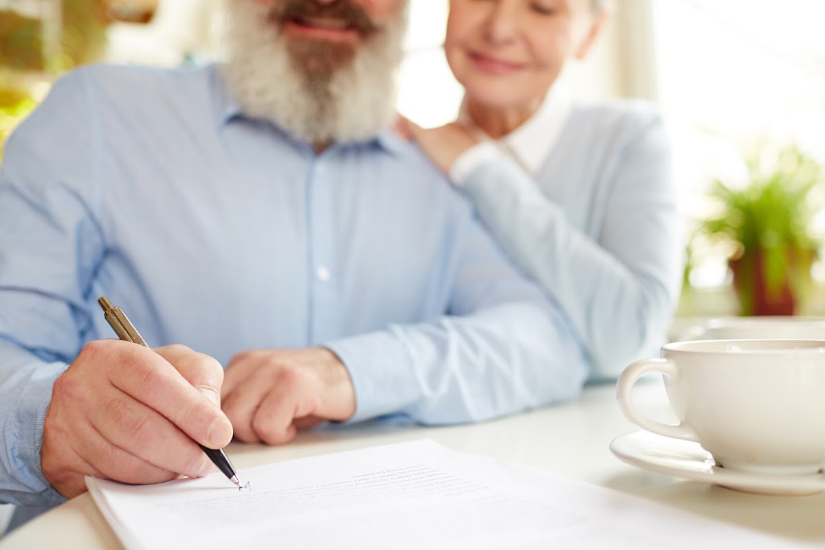 Senior man signing document with woman nearby