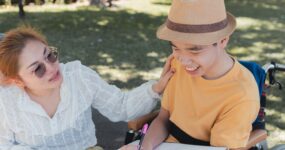 Young man in wheelchair drawing with woman outdoors