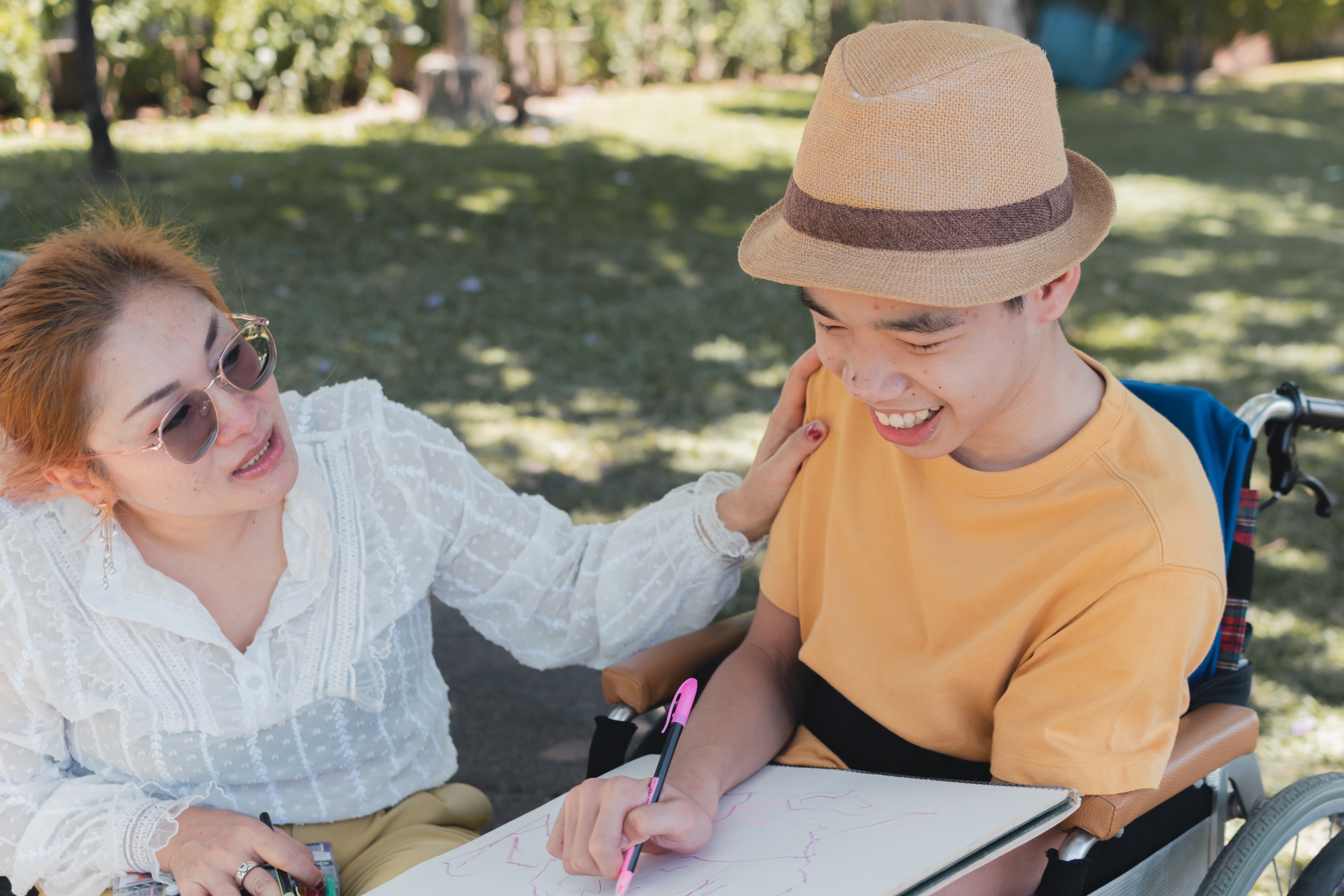 Young man in wheelchair drawing with woman outdoors